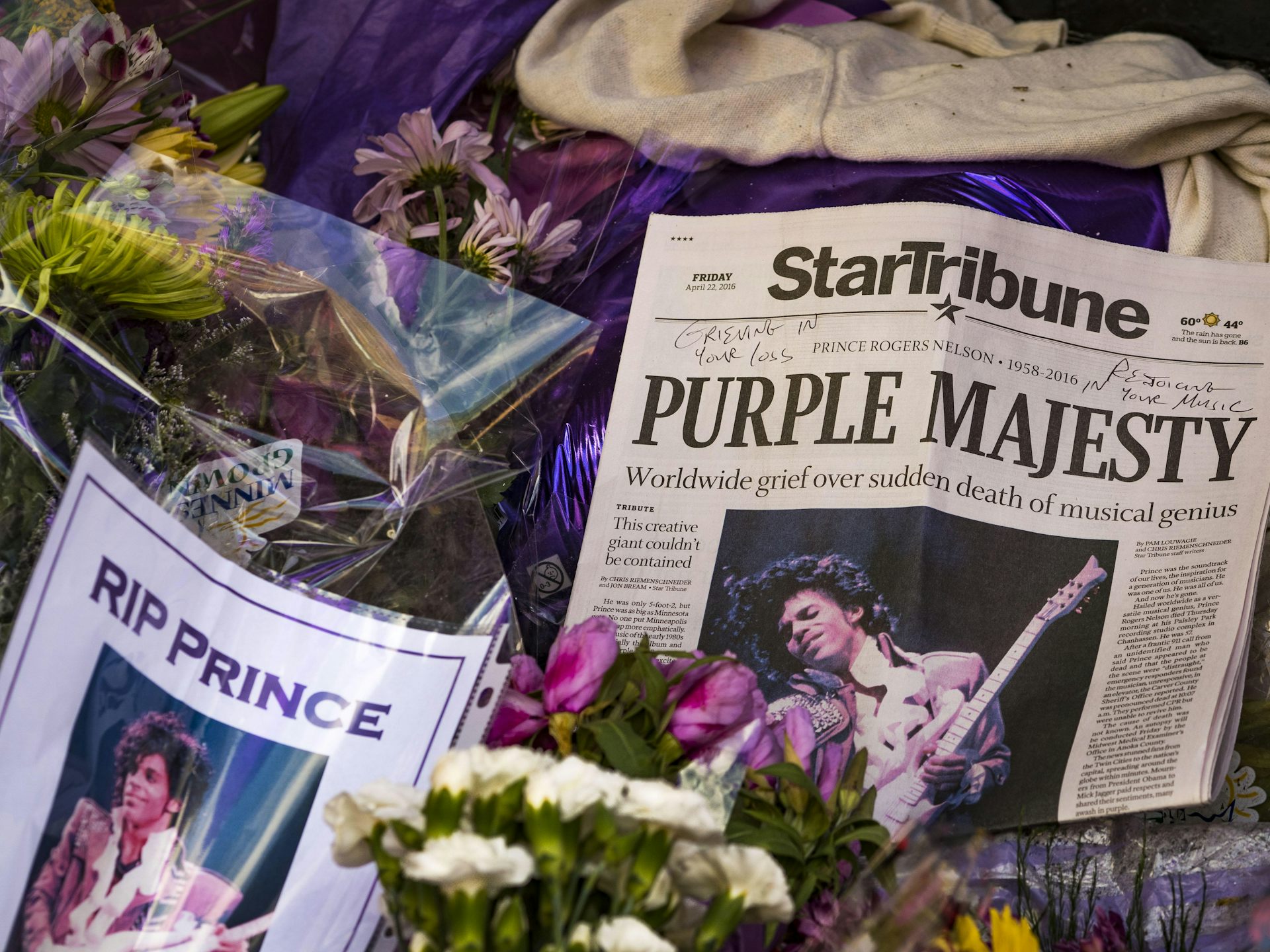 Memorial for the artist Prince with newspaper cuttings from the day of his death, flowers and a sign that says 'RIP Prince'